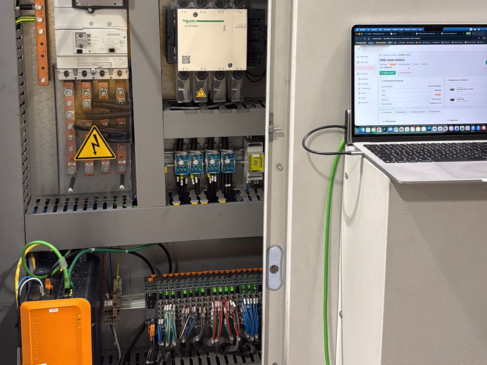 Quadro elettrico in reparto con accanto un portatile con il software Light-MES Discreto aperto su un ordine di produzione